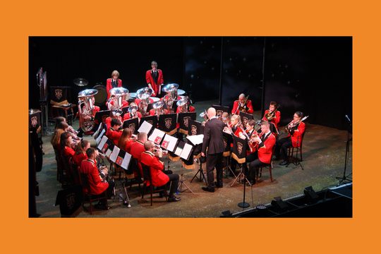 A brass band wearing red jackets perform on a stage.