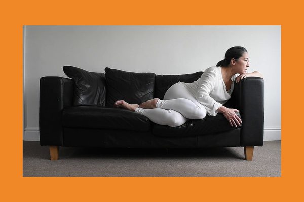 A white, brunette woman wearing all white lies on a black leather sofa.
