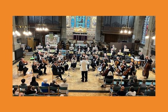 An orchestra wearing black playing in a church to an audience.