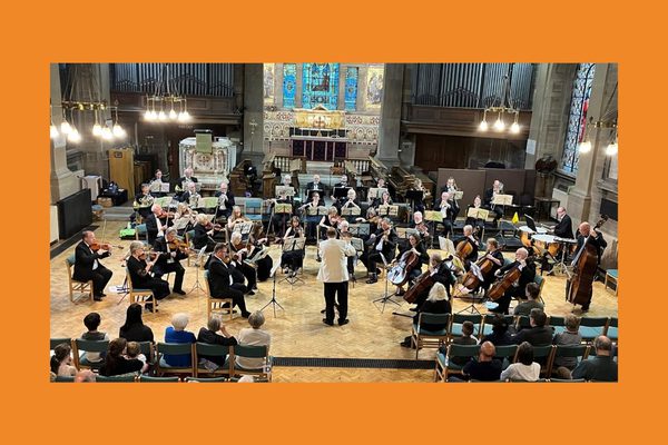 An orchestra wearing black playing in a church to an audience.