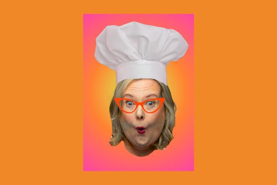 A blonde woman wearing orange glasses and a chef's hat pouting her lips.