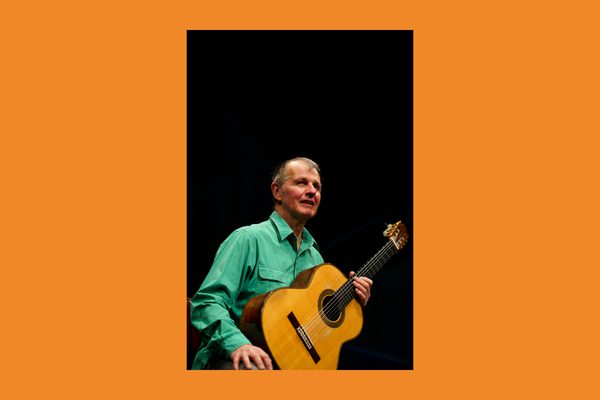An older white man wearing a bright green shirt holding an acoustic guitar.