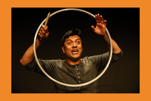 A man with dark hair wearing a long-sleeved grey t-shirt holds up a large metal circle around his face.
