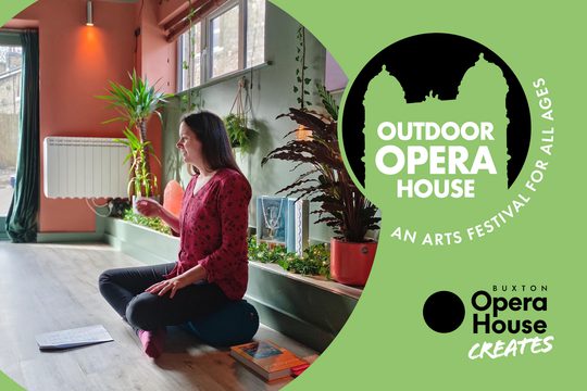 A woman in a red top sits cross legged on the floor in a room full of indoor plants.
