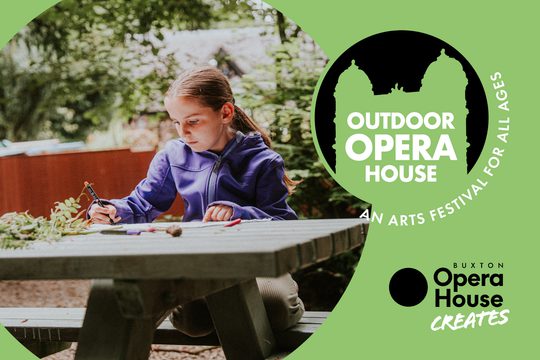 A young girl in a purple raincoat sitting at a picnic bench and drawing.