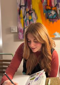 A woman with ginger hair drawing in a sketchbook.