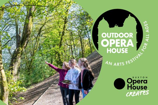 Three girls in the woods pointing at artwork and smiling.