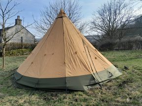 A beige and green tipi in a field.