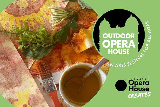 A table stained with orange paint with leaves and a paintbrush. Outdoor Opera House logo. Buxton Opera House Creates logo.