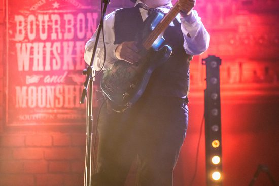 A man in a cowboy hat playing the guitar with red lights around him.