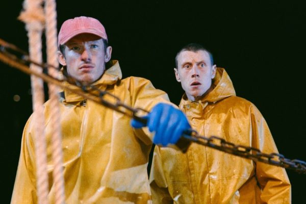 Two men on a boat at night time. They are wearing yellow waterproof jackets and blue gloves, and look scared.
