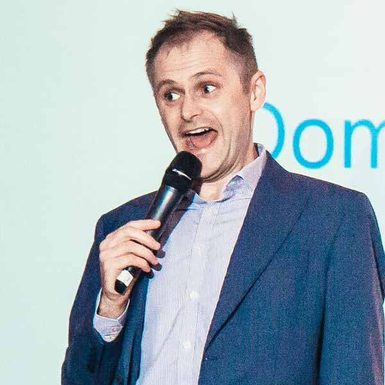 A man in a blue suit holds a microphone and pulls a funny face.