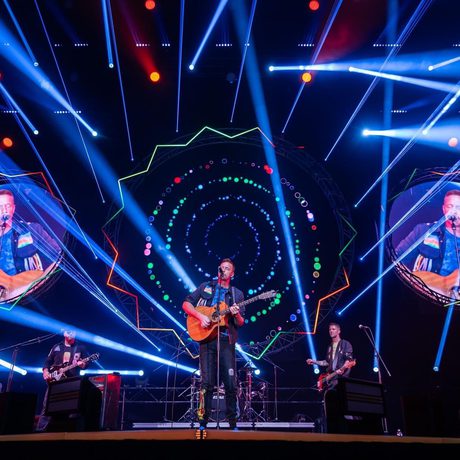 A band on a stage with lights and lasers around them.