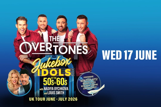 Four men in red jackets and white t-shirts stand behind a blue jukebox with a neon yellow sign that says Jukebox Idols.