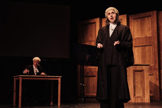 A woman dressed as a judge in a black robe and wig addressing the jury