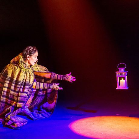 A girls with brown hair wearing a large cape with a hood makes a lantern float.