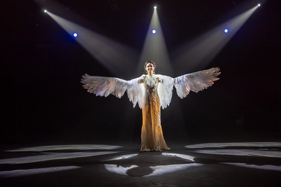 A woman in a gold dress with large white feathered wings.