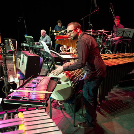 A man playing various percussion instruments, such as a large drum, a xylophone, and a glockenspiel.