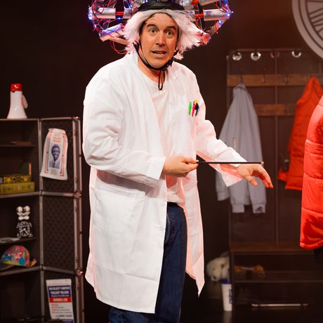 A man in a white lab coat with a scientific contraption strapped to his head. It is a tangle of tubes and wires.