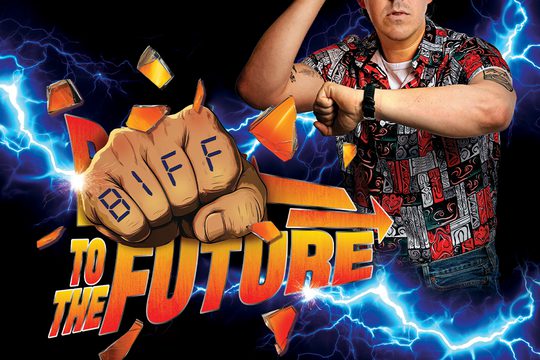 A man in a red, white and black shirt with an array of patterns. He is looking at his watch.