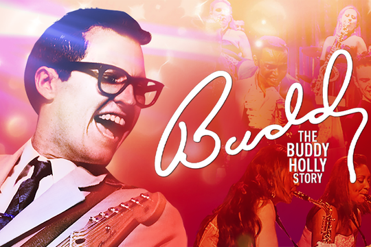 Buddy Holly smiling widely playing the guitar