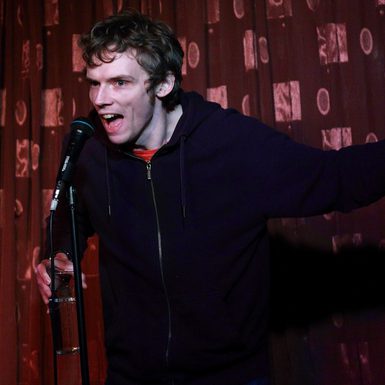 A man wearing all black stands on a stage and points to the right.