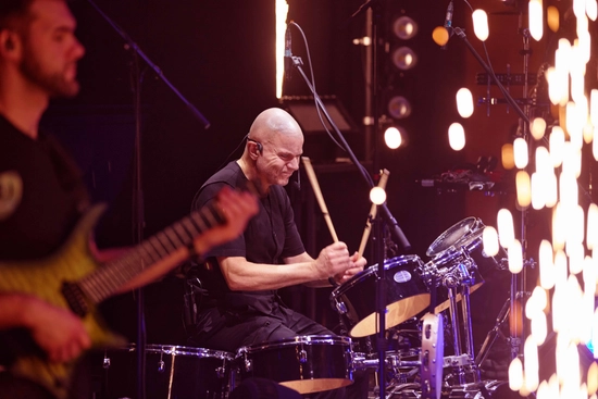 A man playing the drums. There are gold fireworks on the stage.