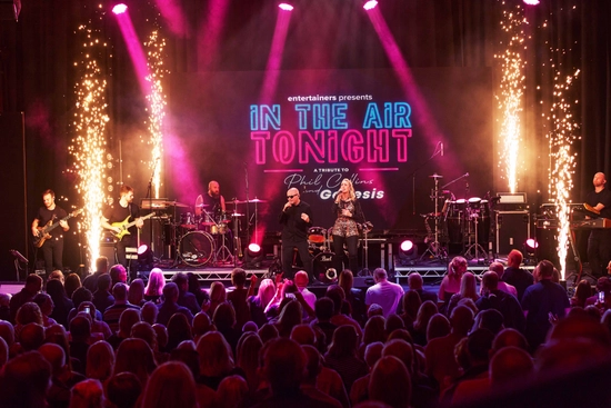 A man and a woman on stage singing. They are surrounded by pink spotlights and gold fireworks.