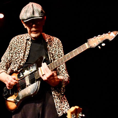 Man in cap and Leppard print shirt plays electric guitar