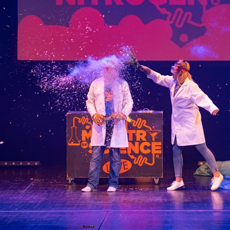 Two people in a lab coat. The person on the right is throwing something into the other person's face.