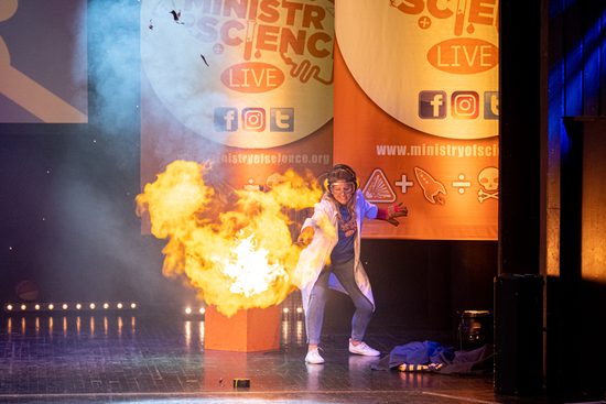 A woman in a lab coat setting something on fire.