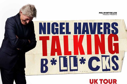 Nigel Havers crossing his arms and laughing.