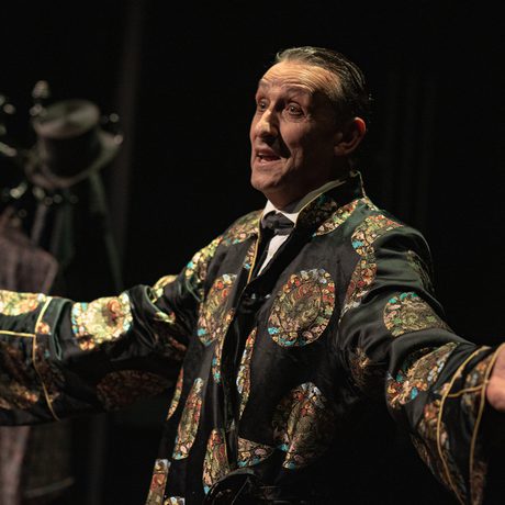 A man in a colourful robe standing with his hands out to the sides.