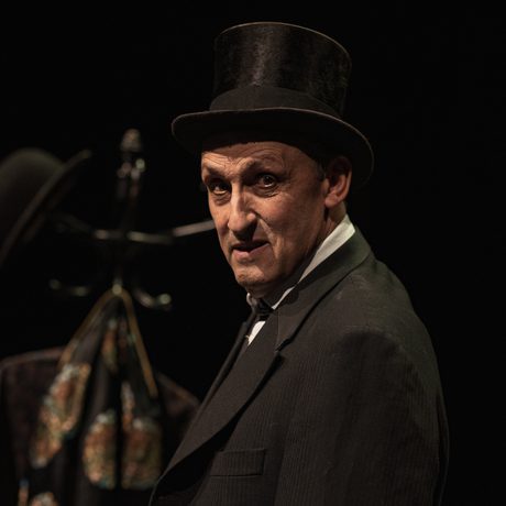 A man in a black suit, wearing a black top hat.