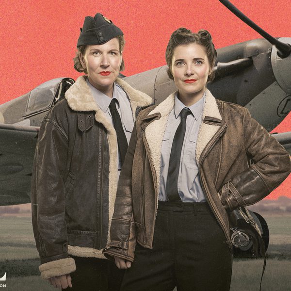 Two women dressed in fleece lined leather jackets stand in front of a spitfire