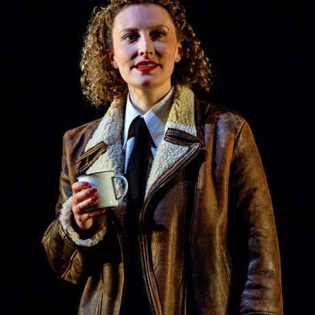 Woman in fleece lined leather jacket and red lipstick holds a mug