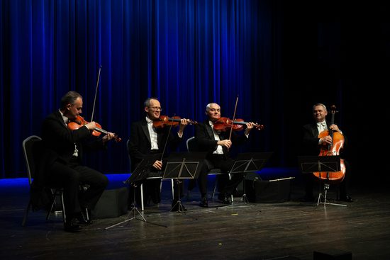 A string quartet playing on a stage wearing black suits and white shirts