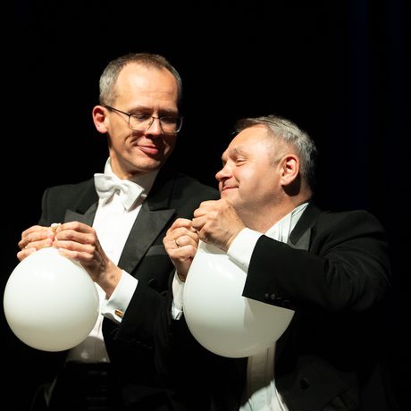 Two men smiling holding white balloons.