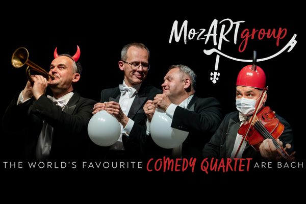 Four men in black suits and white shirts playing instruments in funny ways, for example with things on their heads.