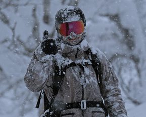 A person in a full ski suit and goggles covered in snow.