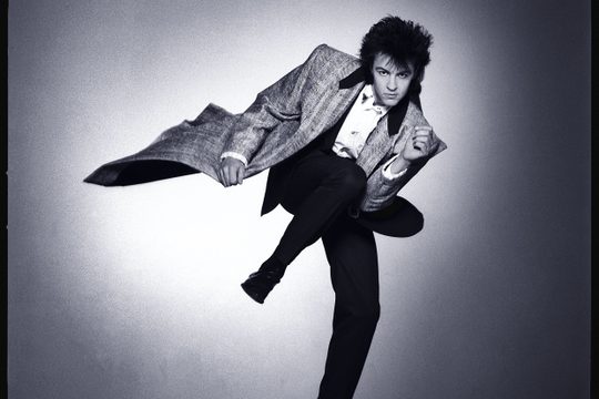 Black and white: man with 80's haircut dances in long jacket