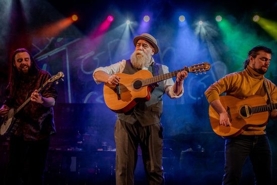 Three men standing in a line playing guitars.