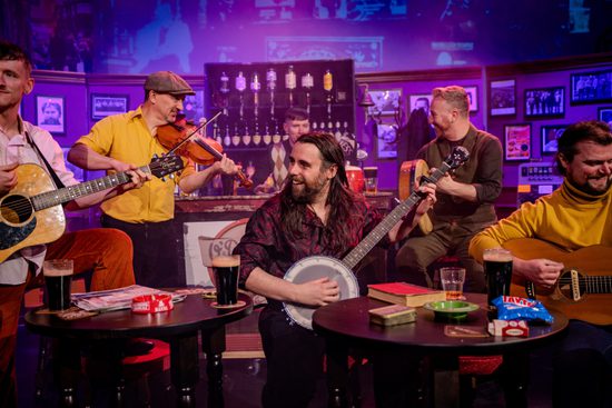 Male musicians sit in a pub playing musical instruments.