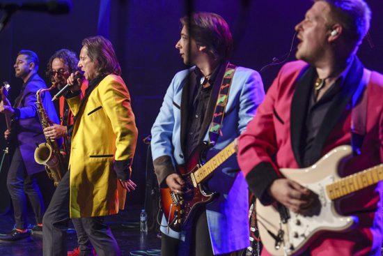 Musicians in brightly coloured jackets stand in a line playing to their audience