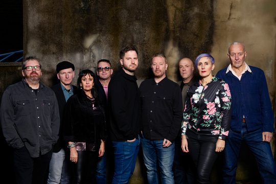 Nine people stand in a line and look straight towards the camera.