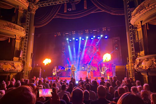 A crowd looking at a stage. On the stage is a singer, band, spotlights, and fire.