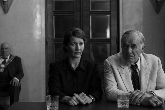 Black and white image of a man and a woman sat next to each other in front of a large wooden door.