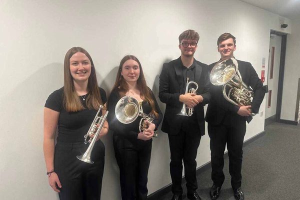 Two young men and two young women wearing black and holding brass instruments.