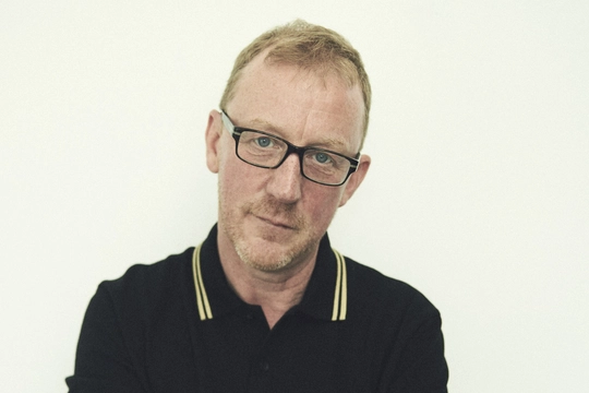 Dave Rowntree a man with ginger hair and light stubble looks into camera wearing dark rimmed classes and a black polo neck