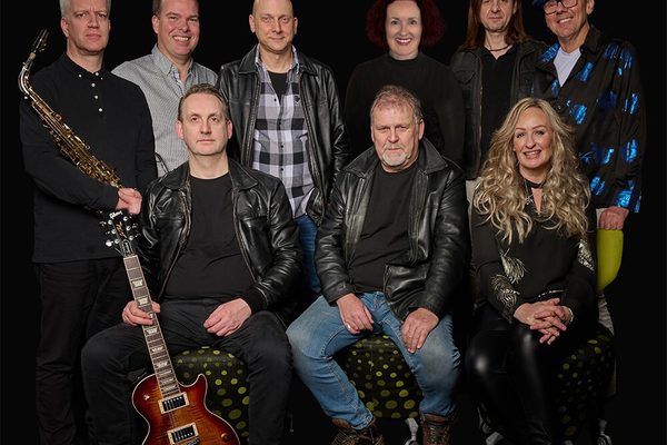 Nine musicians pose infront of a black background holding their instruments.